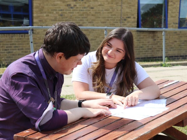 Two students sitting at bench chatting.