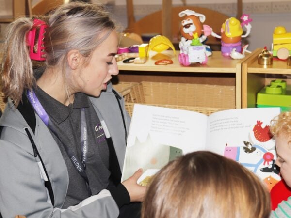 Student reading a children's book to nursery children.