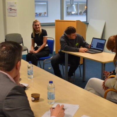Student presenting to judges on a computer for his new coffee brand idea. Judges looking at his computer screen.